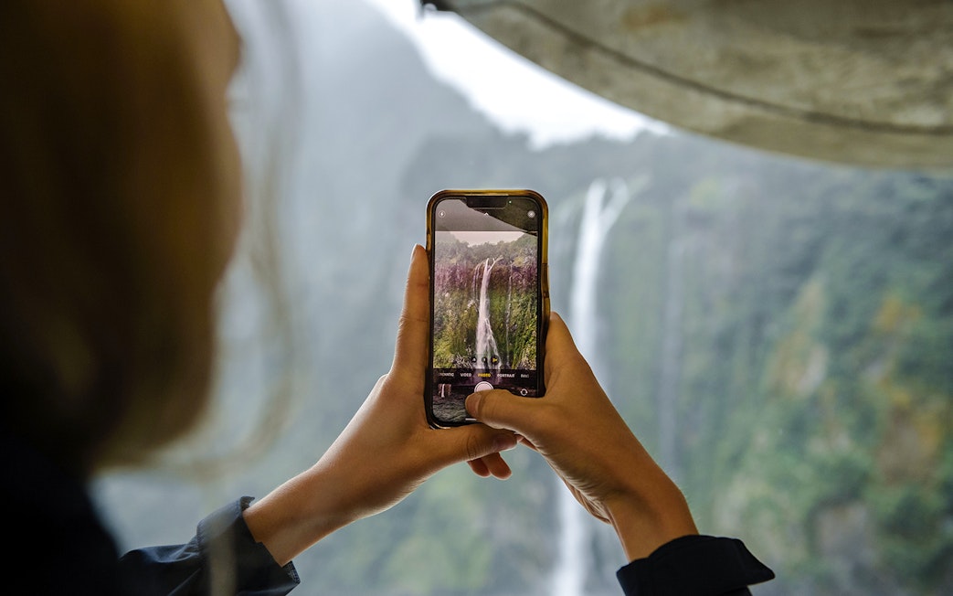 Visitor photographing waterfall at Milford Sound.