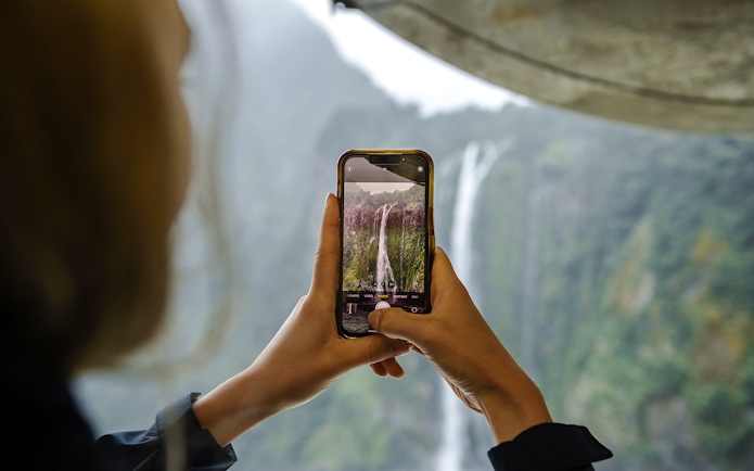 Visitor photographing waterfall at Milford Sound.