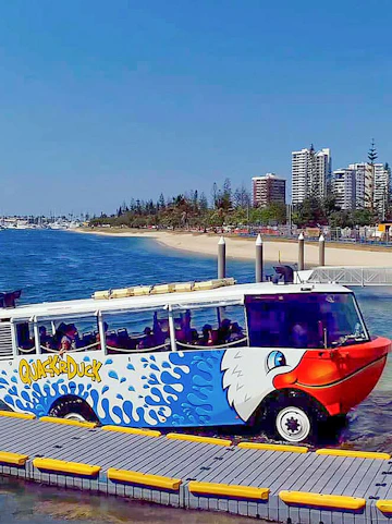 Quack'R Duck amphibious vehicle on a beachside dock with city skyline in the background.