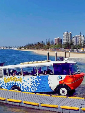 Quack'R Duck amphibious vehicle on a beachside dock with city skyline in the background.