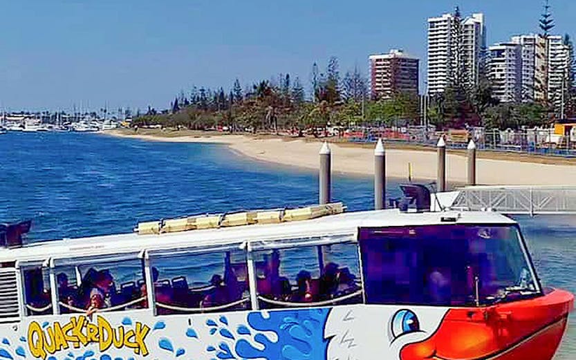Quack'R Duck amphibious vehicle on a beachside dock with city skyline in the background.
