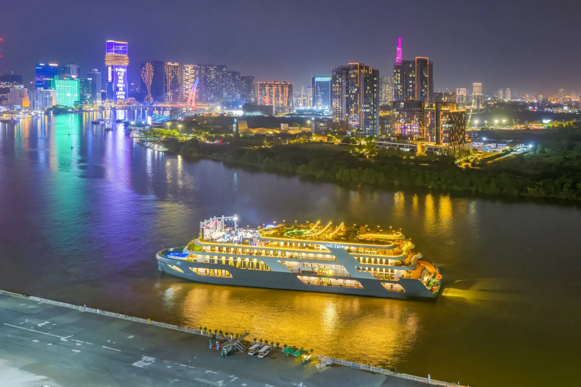Luxury cruise ship on Saigon River at night, Ho Chi Minh City skyline in background.