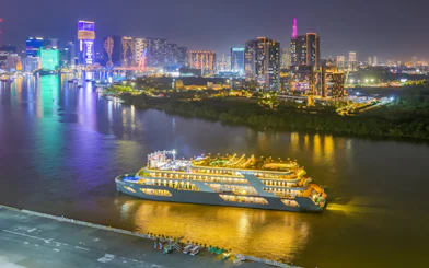 Luxury cruise ship on Saigon River at night, Ho Chi Minh City skyline in background.