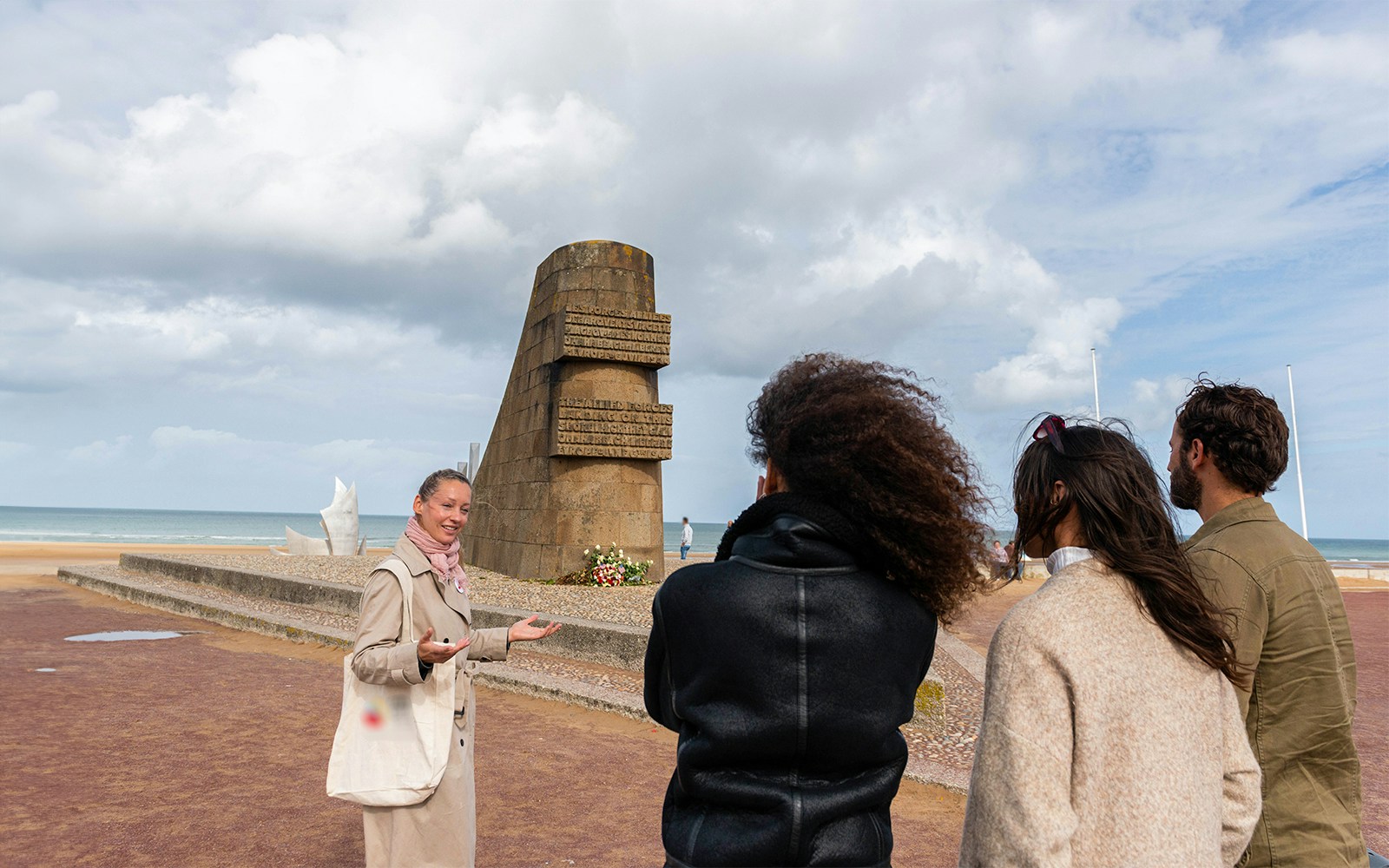 Guide with visitors at Omaha Beach Memorial, Normandy, discussing historical significance.