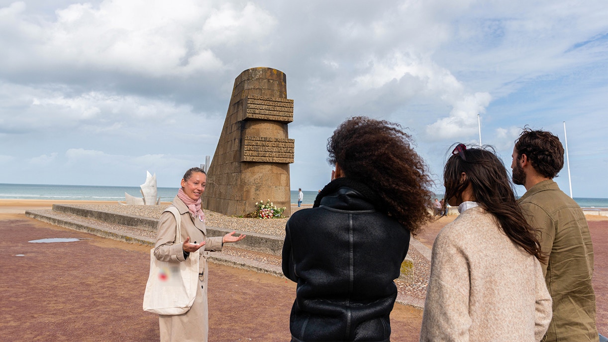 Guide with visitors at Omaha Beach Memorial, Normandy, discussing historical significance.