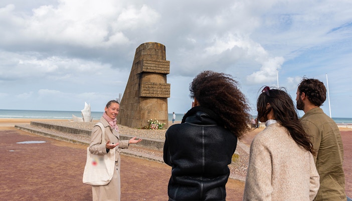 Guide explaining Omaha Beach Memorial to visitors in Normandy.