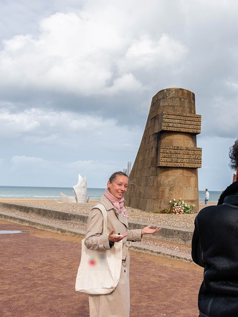 Guide explaining Omaha Beach Memorial to visitors in Normandy.