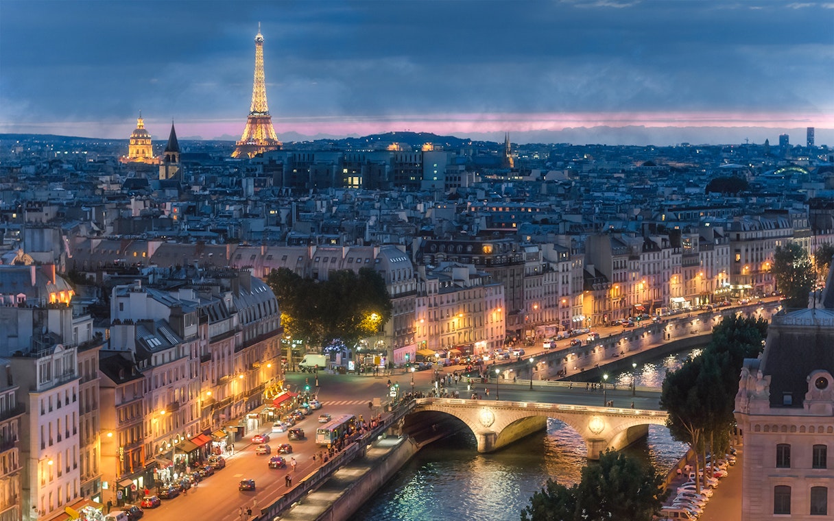 Eiffel Tower and Paris skyline at dusk, view from Seine River bridge.