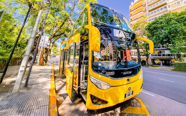 Yellow double-decker tour bus on a tree-lined street in Buenos Aires.