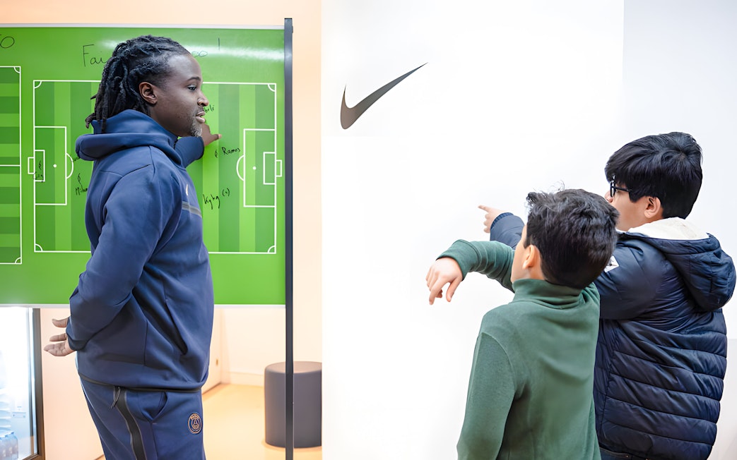 Coach explaining tactics to children at PSG Stadium, Paris, France.