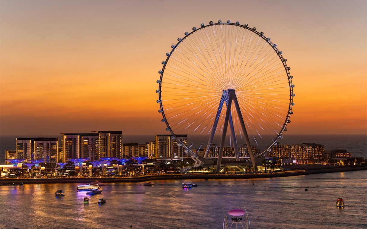 Dubai Ferris wheel at sunset with yachts on the water.