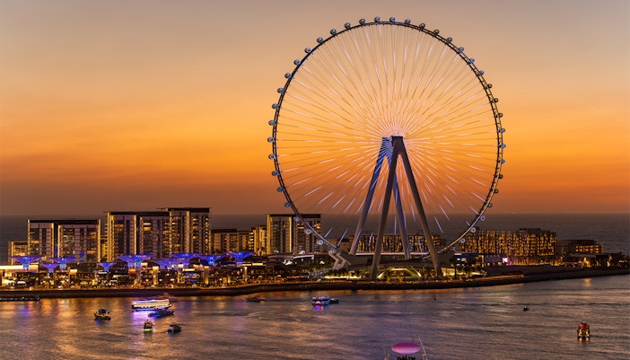 Dubai Ferris wheel at sunset with yachts on the water.