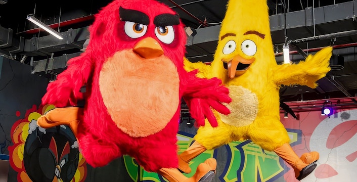 Red and yellow Angry Birds mascots jumping indoors with graffiti background.