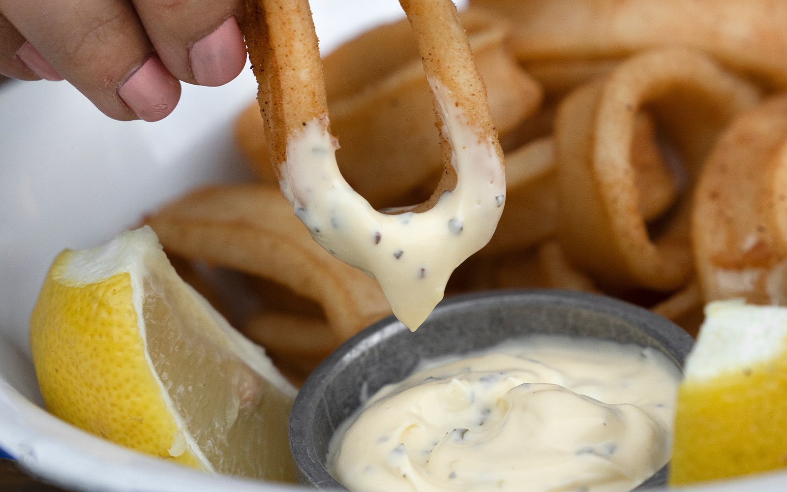 Fried calamari dipped in aioli sauce with lemon wedge at cafe.