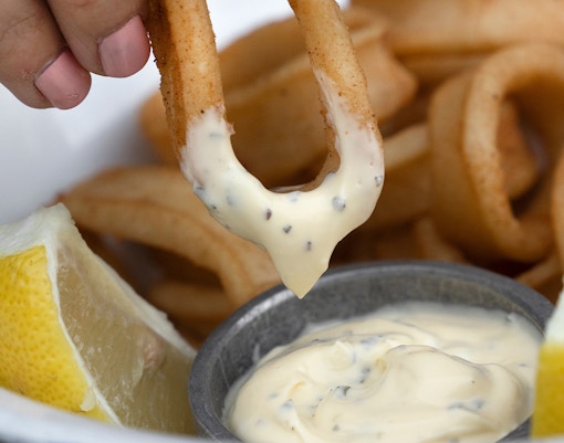 Fried calamari dipped in aioli sauce with lemon wedge at cafe.