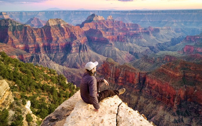 Man sitting on the edge of the Grand Canyon, overlooking vast colorful rock formations.