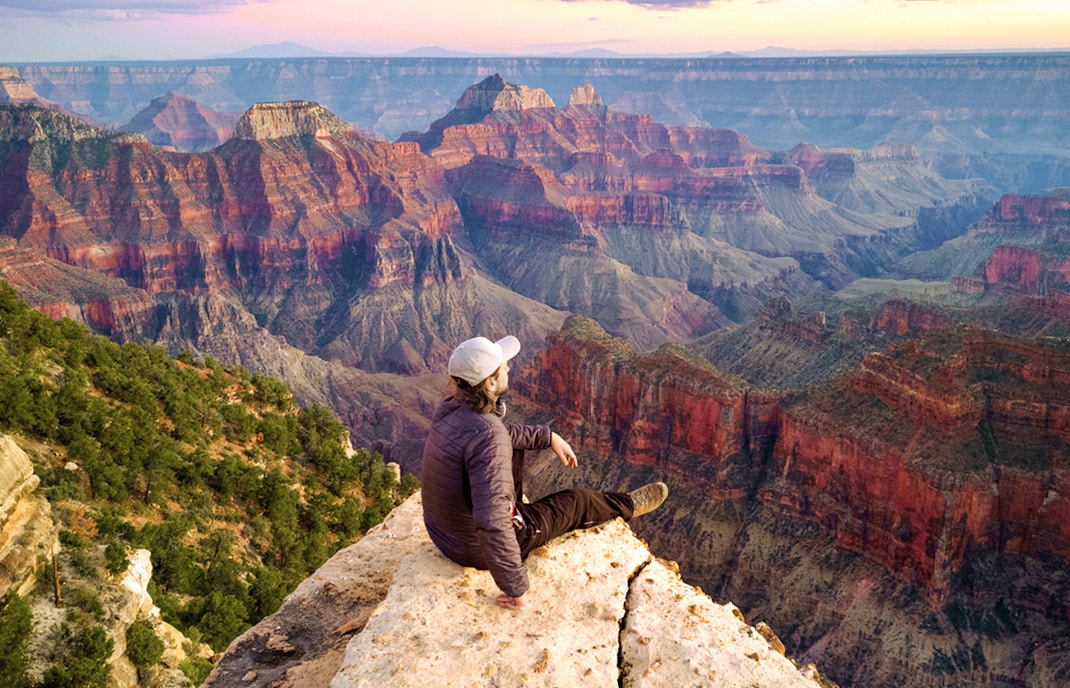Man sitting on the edge of the Grand Canyon, Arizona, overlooking vast canyon landscape.
