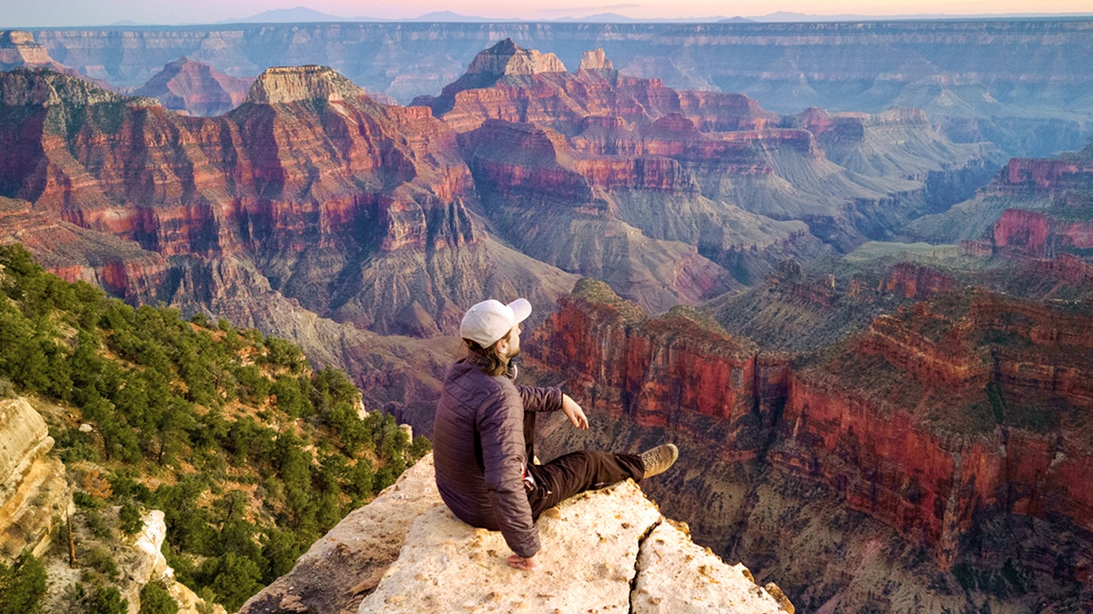 Man sitting on the edge of the Grand Canyon, overlooking vast colorful rock formations.