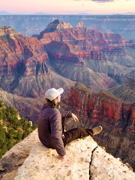 Man sitting on the edge of the Grand Canyon, overlooking vast colorful rock formations.
