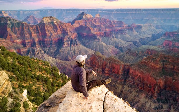 Man sitting on the edge of the Grand Canyon, overlooking vast colorful rock formations.