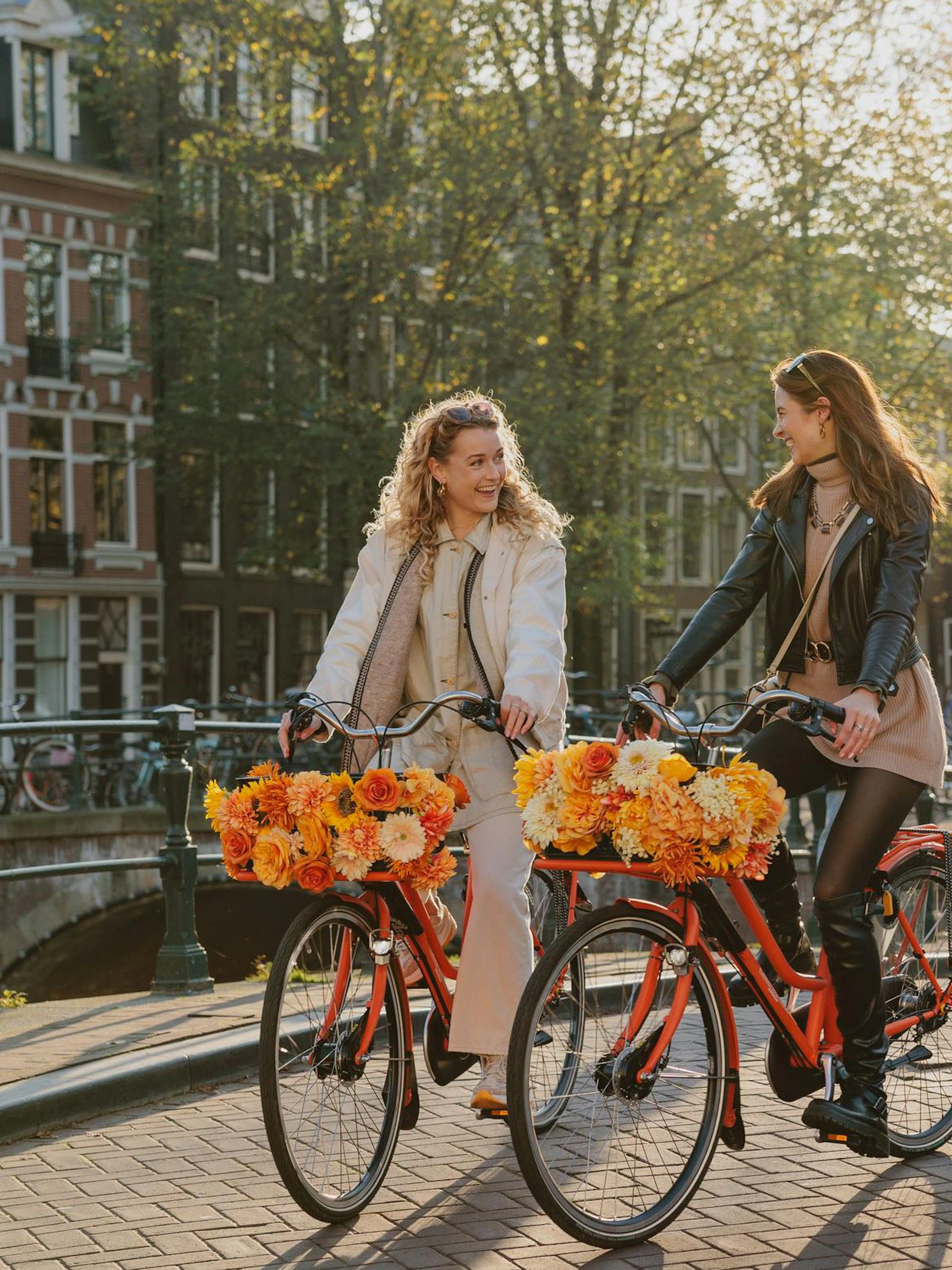 Two people biking along a canal in Amsterdam with flower baskets.