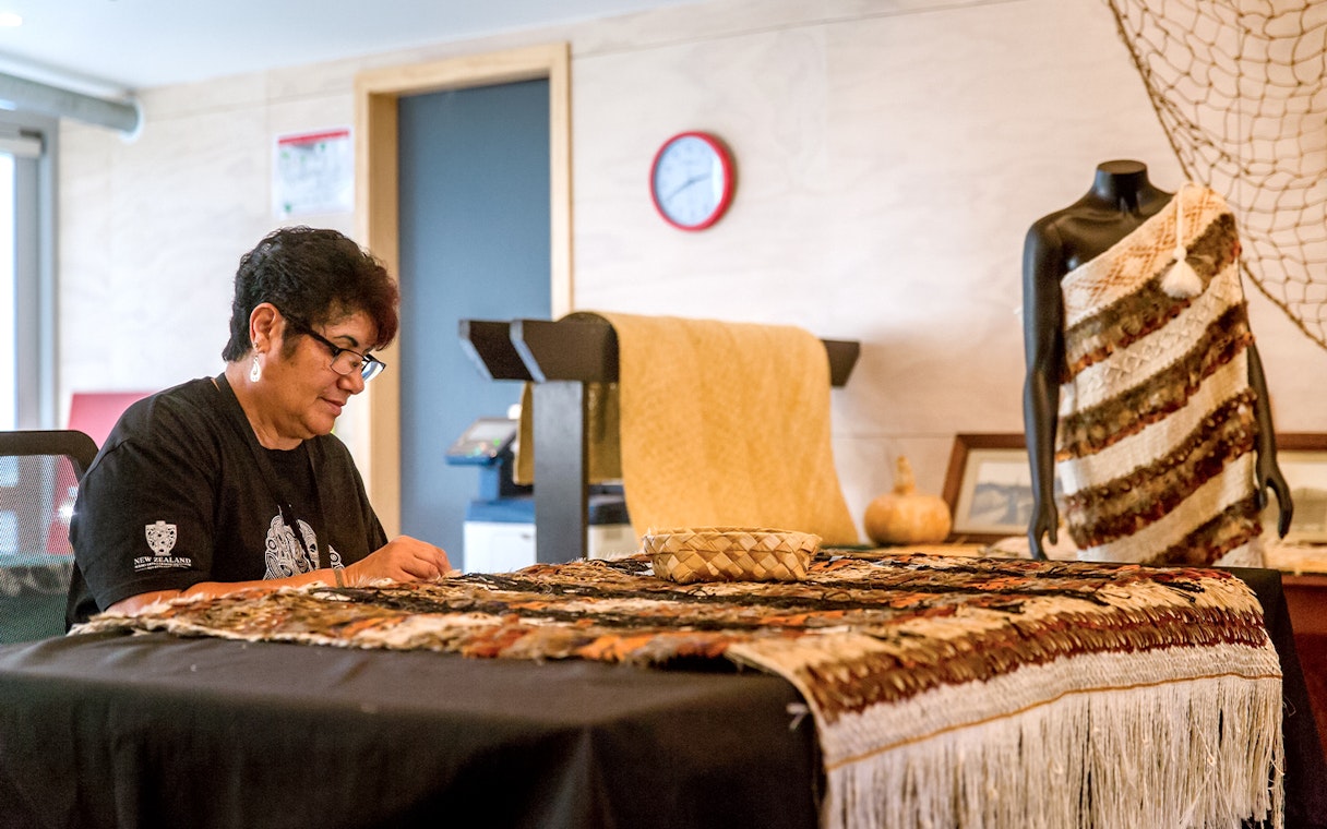Craftsperson weaving traditional Māori garment at Te Puia, New Zealand.