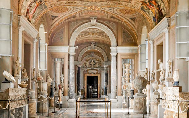 Gallery of the Candelabra in the Vatican Museum with classical sculptures and ornate ceiling.