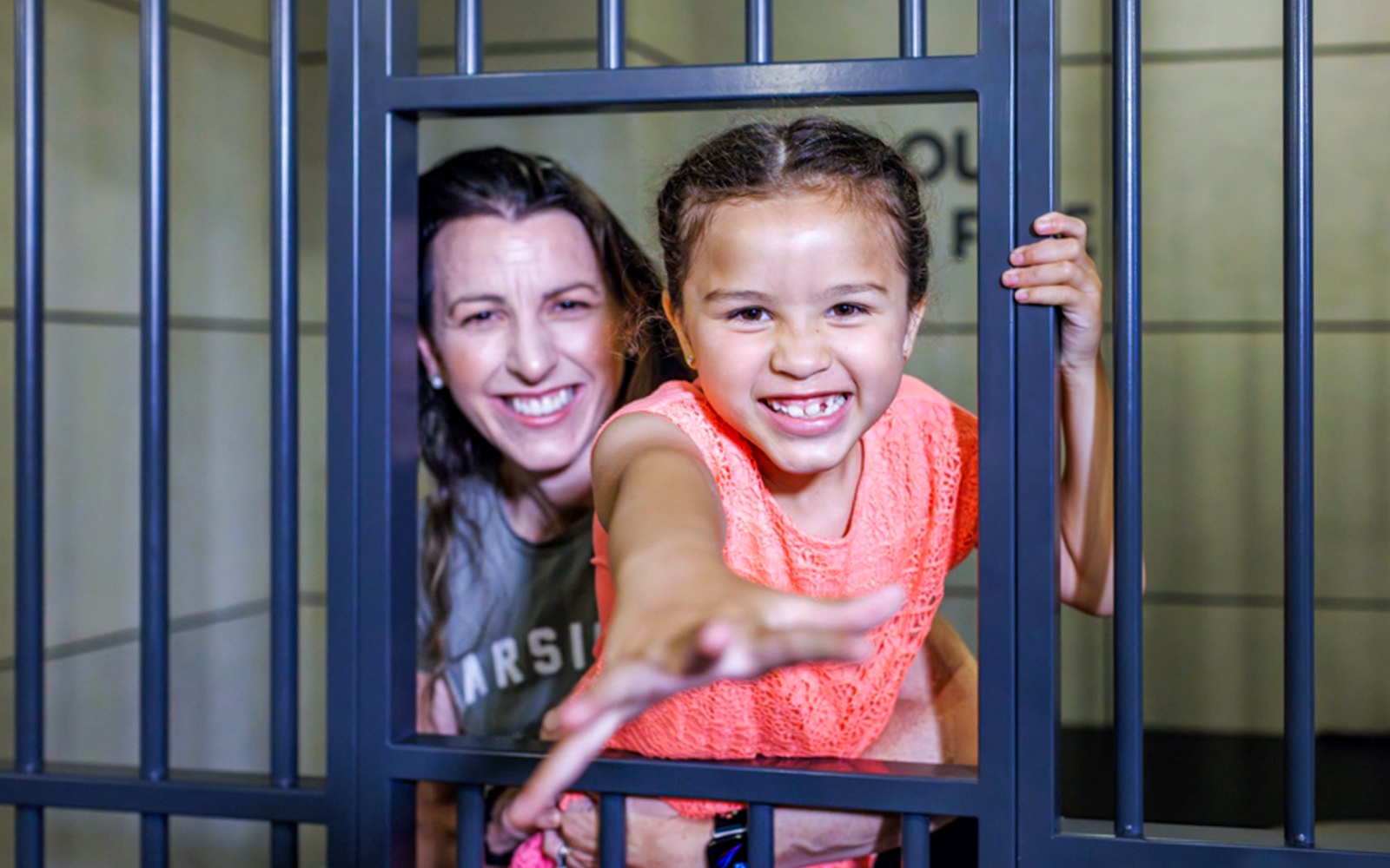 Child and adult smiling behind bars at Monopoly Dreams Melbourne.