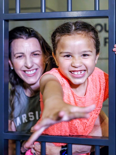 Child and adult smiling behind bars at Monopoly Dreams Melbourne.