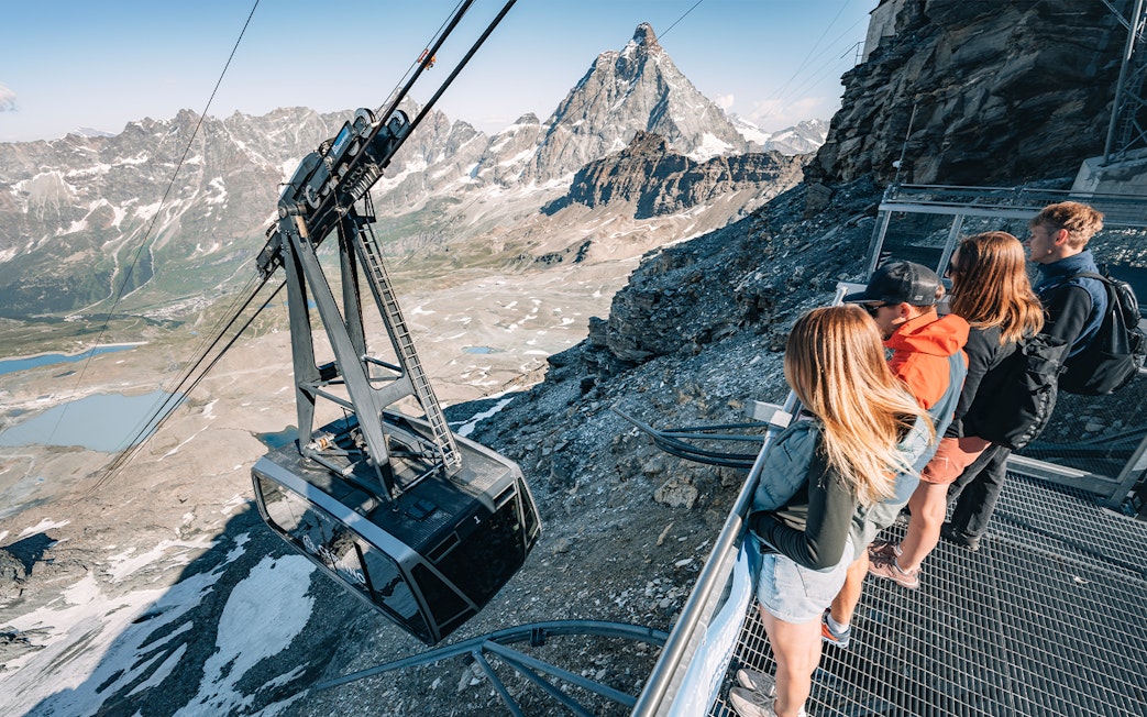 Cable car ascending Glacier with tourists viewing Matterhorn in Swiss Alps.
