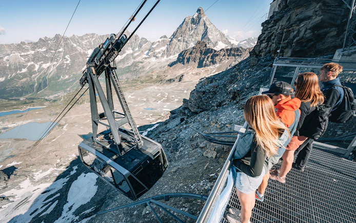 Cable car ascending Glacier with tourists viewing Matterhorn in Swiss Alps.