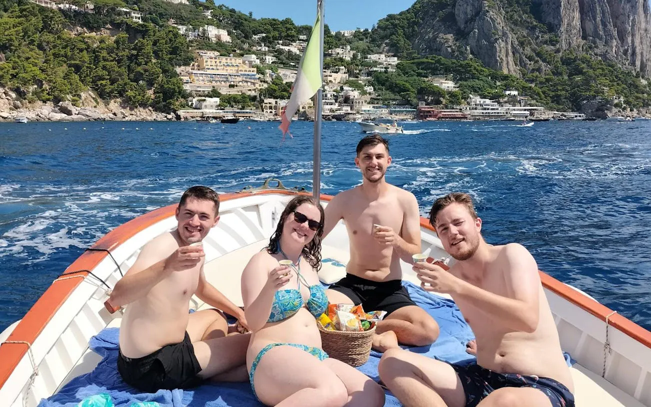 Tourists enjoying snacks and limoncello on a boat near Capri's coastline.