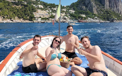 Tourists enjoying snacks and limoncello on a boat near Capri's coastline.