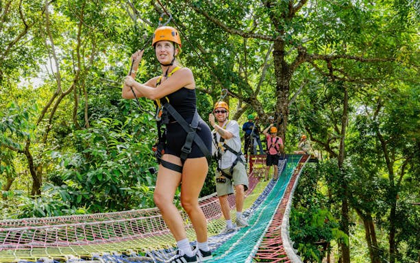 Participants ziplining through lush forest at SKY ROCK eco-adventure in Thailand.