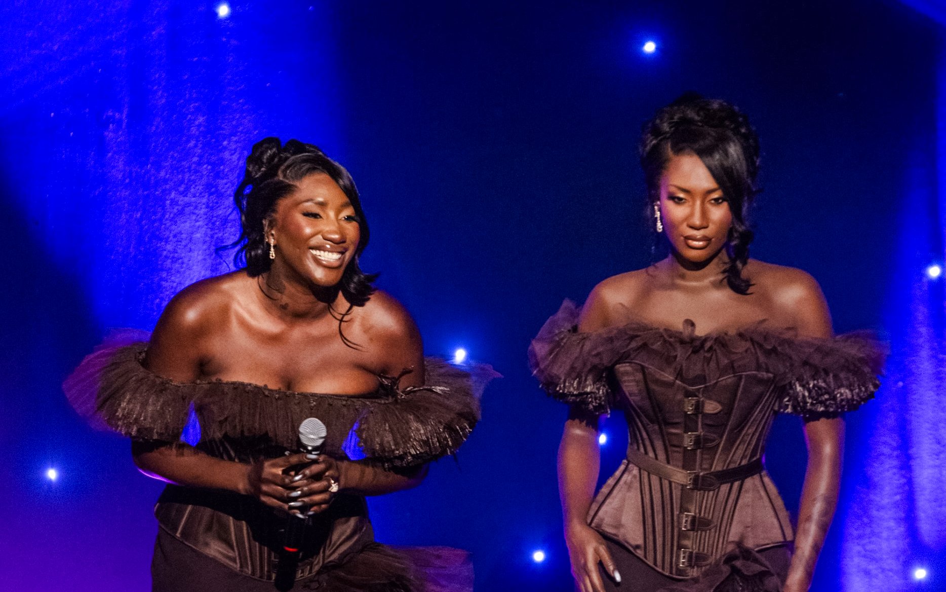 Two women in elegant dresses on stage at Grévin Paris Wax Museum event.