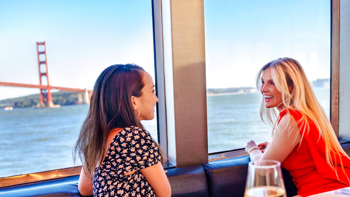 Two women enjoying a view of the Golden Gate Bridge from a San Francisco dinner cruise.