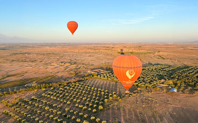 Hot air balloons floating over Marrakech landscape with fields and distant mountains.