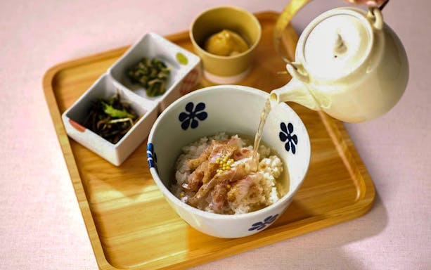 Japanese rice bowl with tea being poured, served with side dishes on a wooden tray.