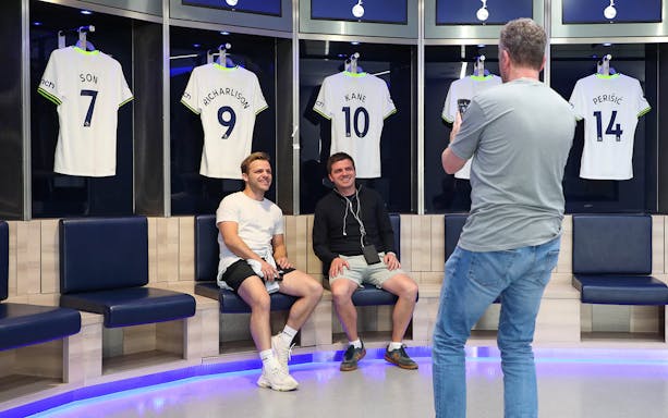 Visitors in Tottenham Hotspur Stadium locker room with player jerseys displayed.