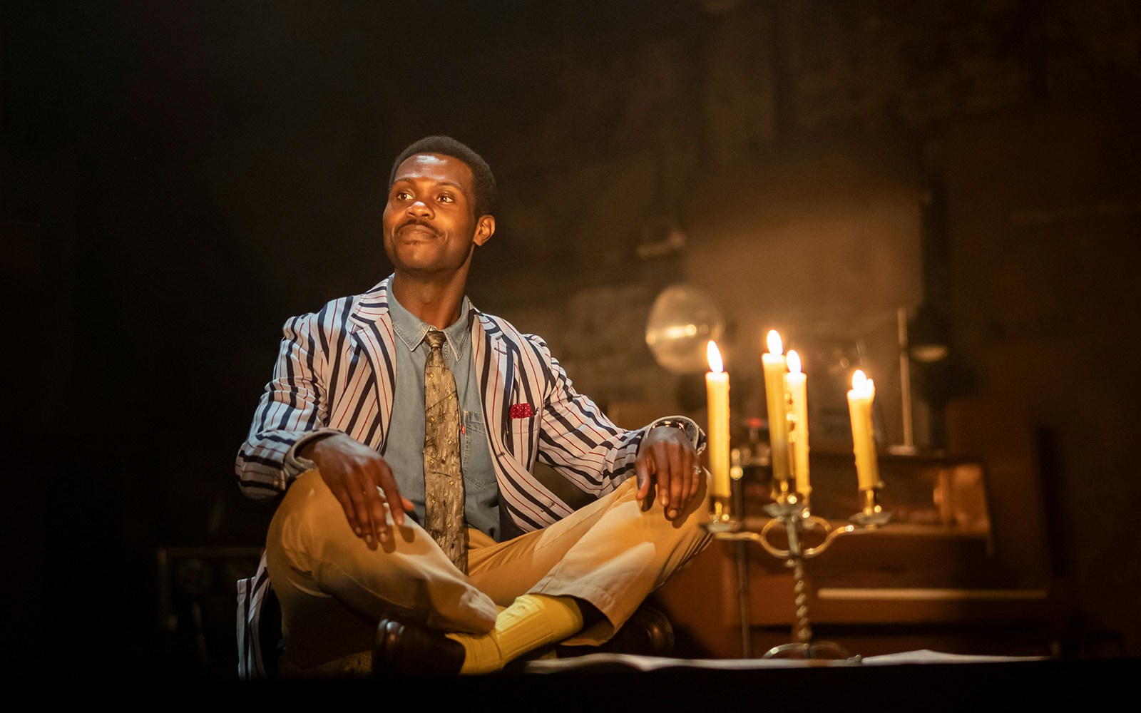 Man in striped jacket sitting near lit candles during "The Glass Menagerie" performance.