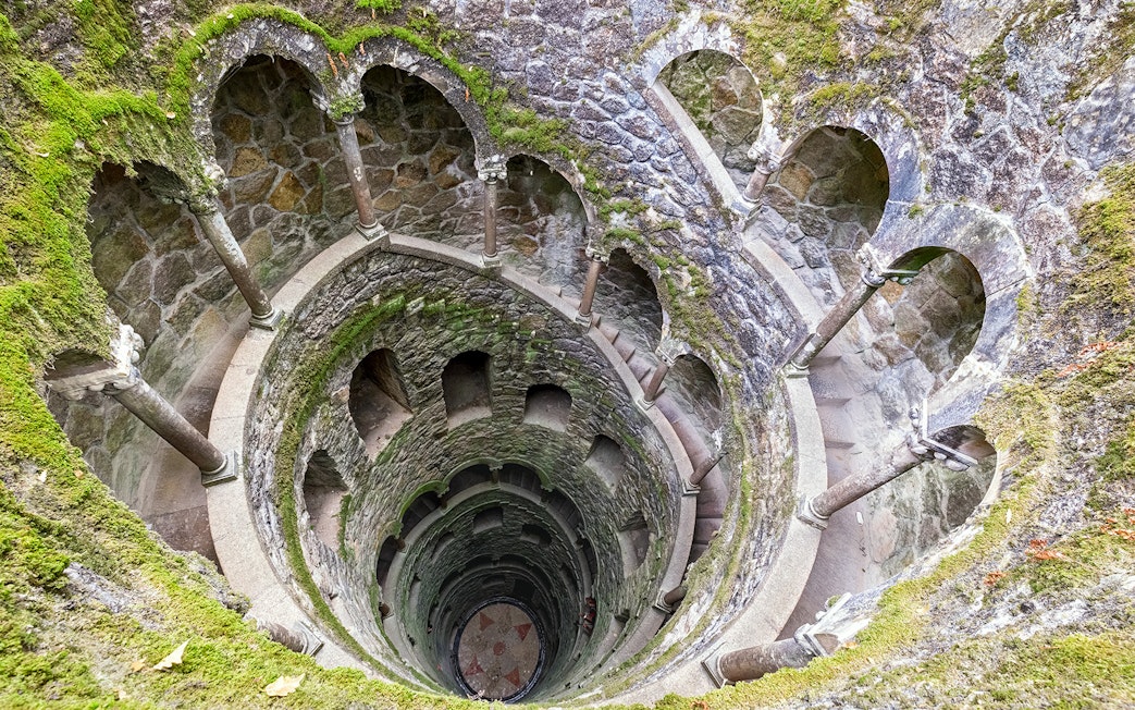 Tour group exploring the spiral staircase of the Initiation Well at Quinta da Regaleira, Sintra, Portugal.