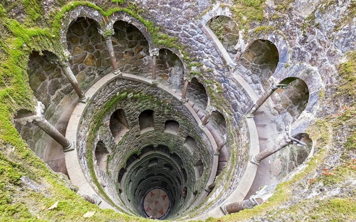 Tour group exploring the spiral staircase of the Initiation Well at Quinta da Regaleira, Sintra, Portugal.