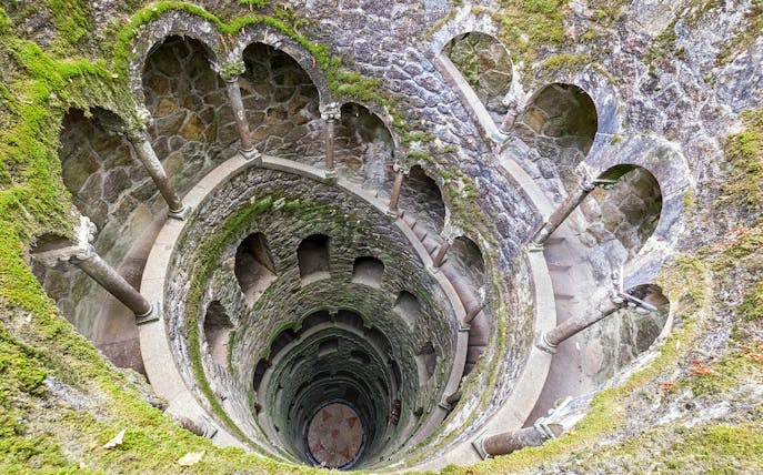 Tour group exploring the spiral staircase of the Initiation Well at Quinta da Regaleira, Sintra, Portugal.
