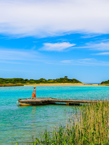 Woman walking on Anglesea River boardwalk with scenic view of water and greenery.