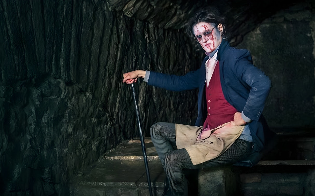Victorian-era actor in makeup and costume in a dimly lit underground setting for paranormal tour.