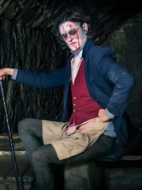 Victorian-era actor in makeup and costume in a dimly lit underground setting for paranormal tour.