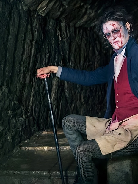 Victorian-era actor in makeup and costume in a dimly lit underground setting for paranormal tour.