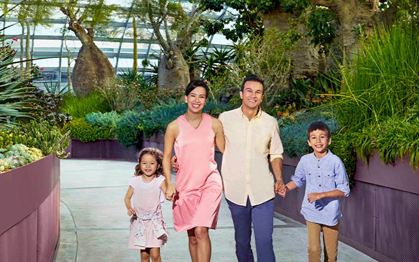 Family walking in Singapore's Gardens by the Bay conservatory, surrounded by lush greenery.