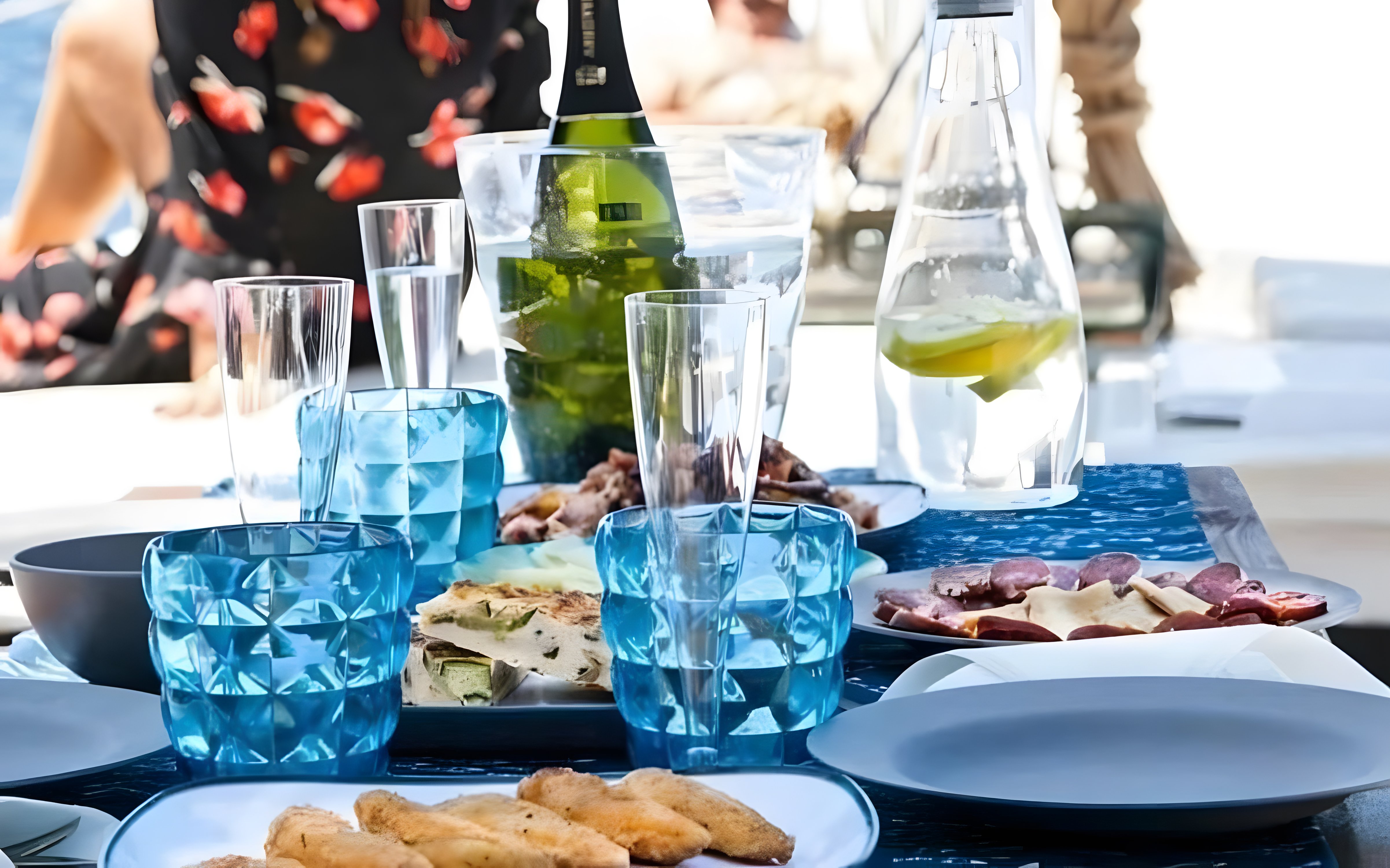 Tapas and drinks set on a cruise boat table with blue glasses and a bottle.