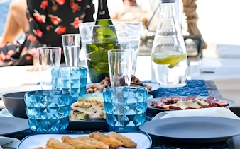 Tapas and drinks set on a cruise boat table with blue glasses and a bottle.
